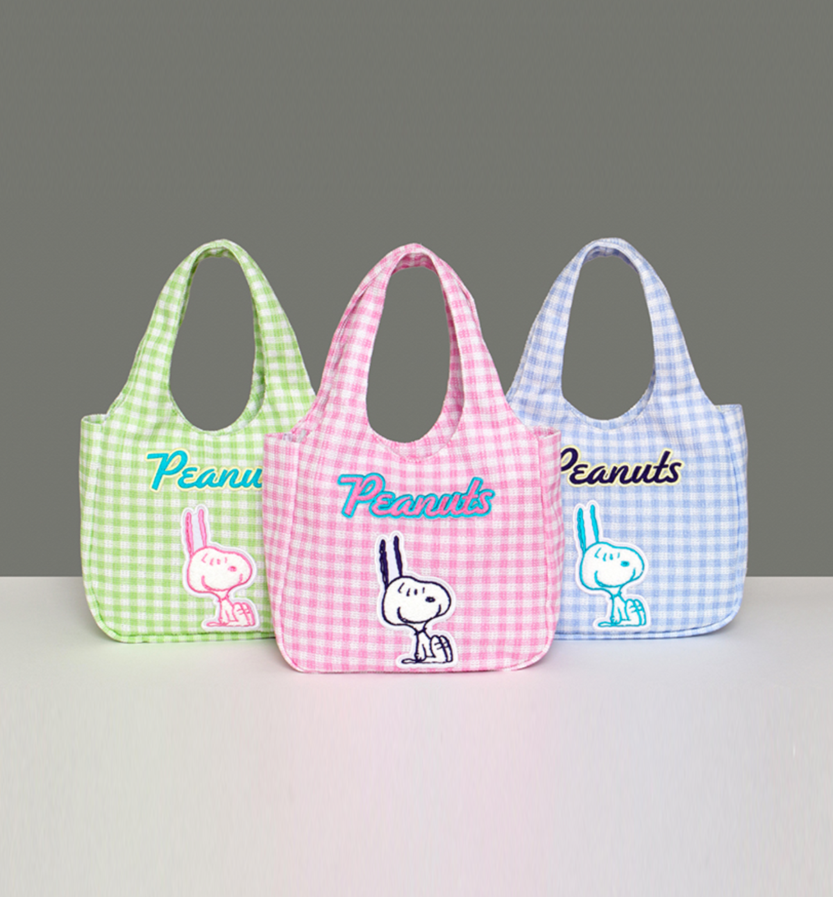 Three gingham bags with 'Peanuts' branding on a gray background