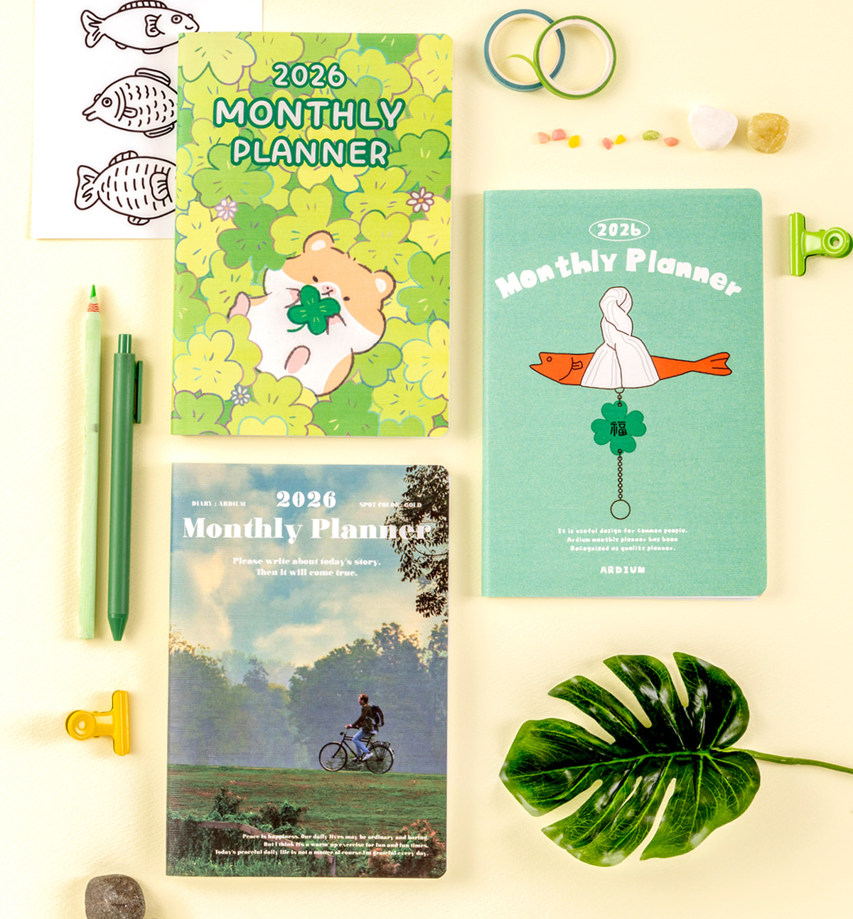 Three 2026 monthly planners with colorful covers on a light surface with stationery items.